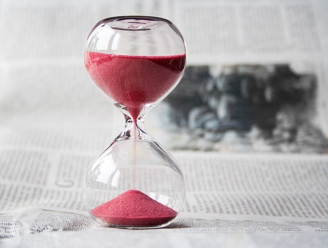 An hourglass with red sand falling from top to bottom. The hourglass is on top of an open newspaper. The image emphasizes the time that passes in the lifespan of a telehandler.