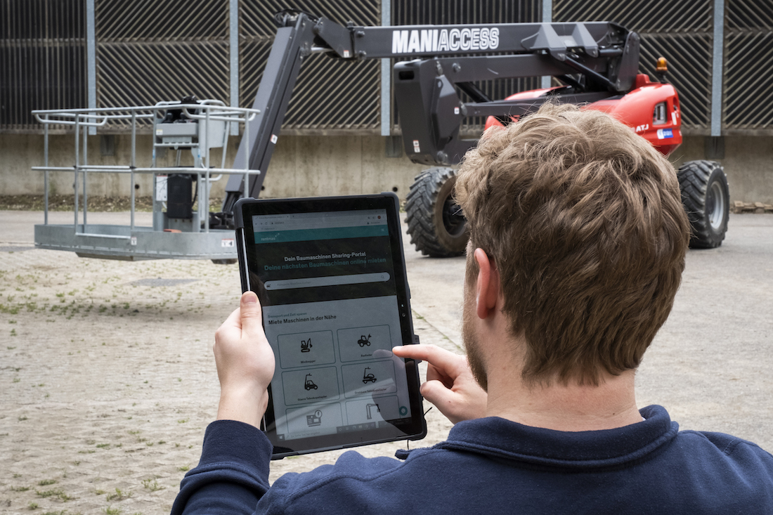 Ein Mitarbeiter eines Bauverleihers steht vor einem Teleskoplader in einem Maschinenpark. Er nutzt ein Tablet, um einen Teleskoplader auf rentmas, einem Online-Portal für Baumaschinenvermietung, zu suchen und zu mieten.